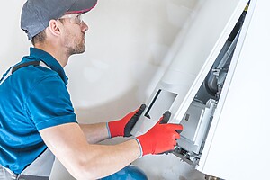 A man wearing a blue shirt and red gloves is repairing a gas boiler, focused on his task.